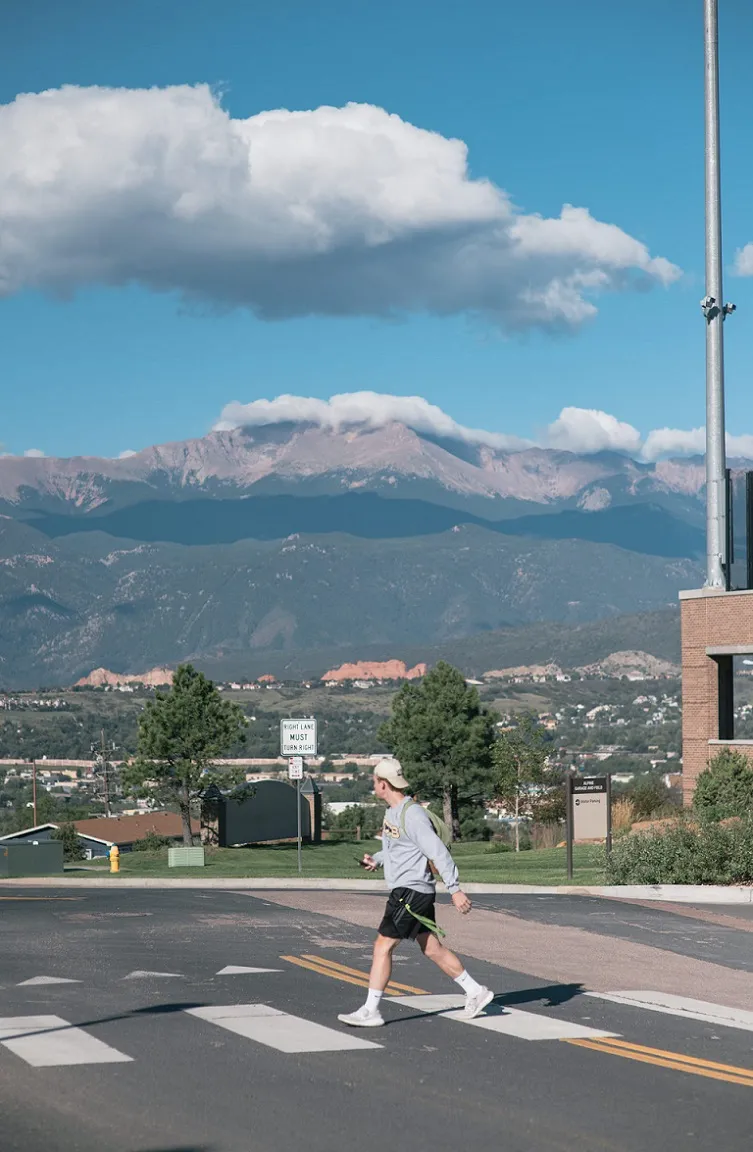 UCCS student walking with Pikes Peak in the background.